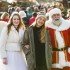 Weihnachtsengel und Weihnachtsmann spazieren über den Weihnachtsmarkt, im Arm eine junge Frau