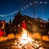 Großes Lagerfeuer mit Menschen drumherum und Lichterkette im Hintergrund