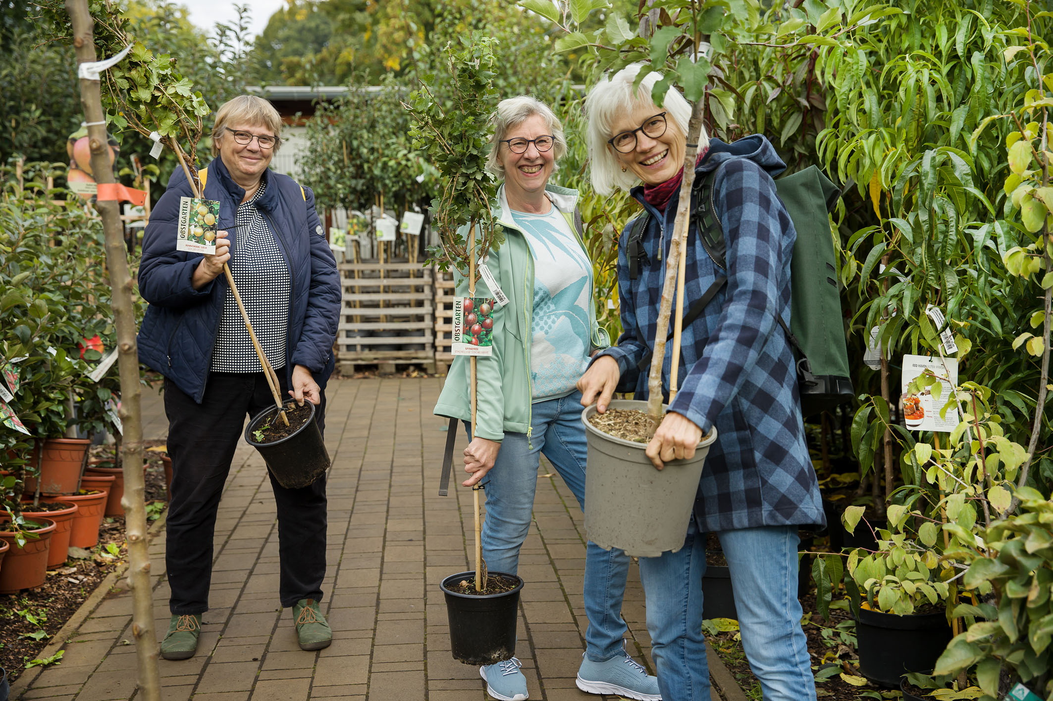 Kundinnen im Pflanzenverkauf mit Obstgehölzen in der Hand.