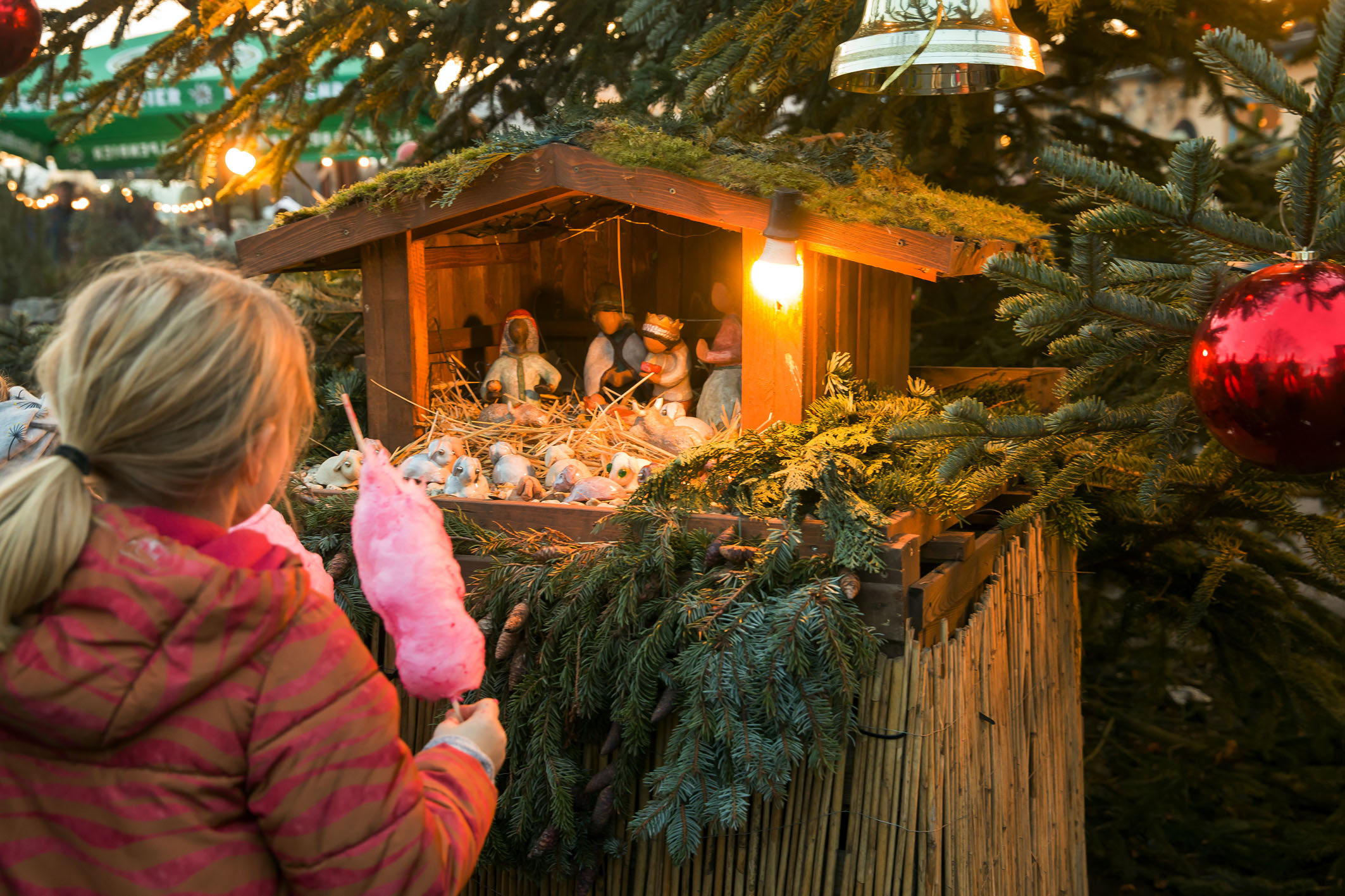 Kind mit rosafarbener Zuckerwatte vor der Weihnachtskrippe